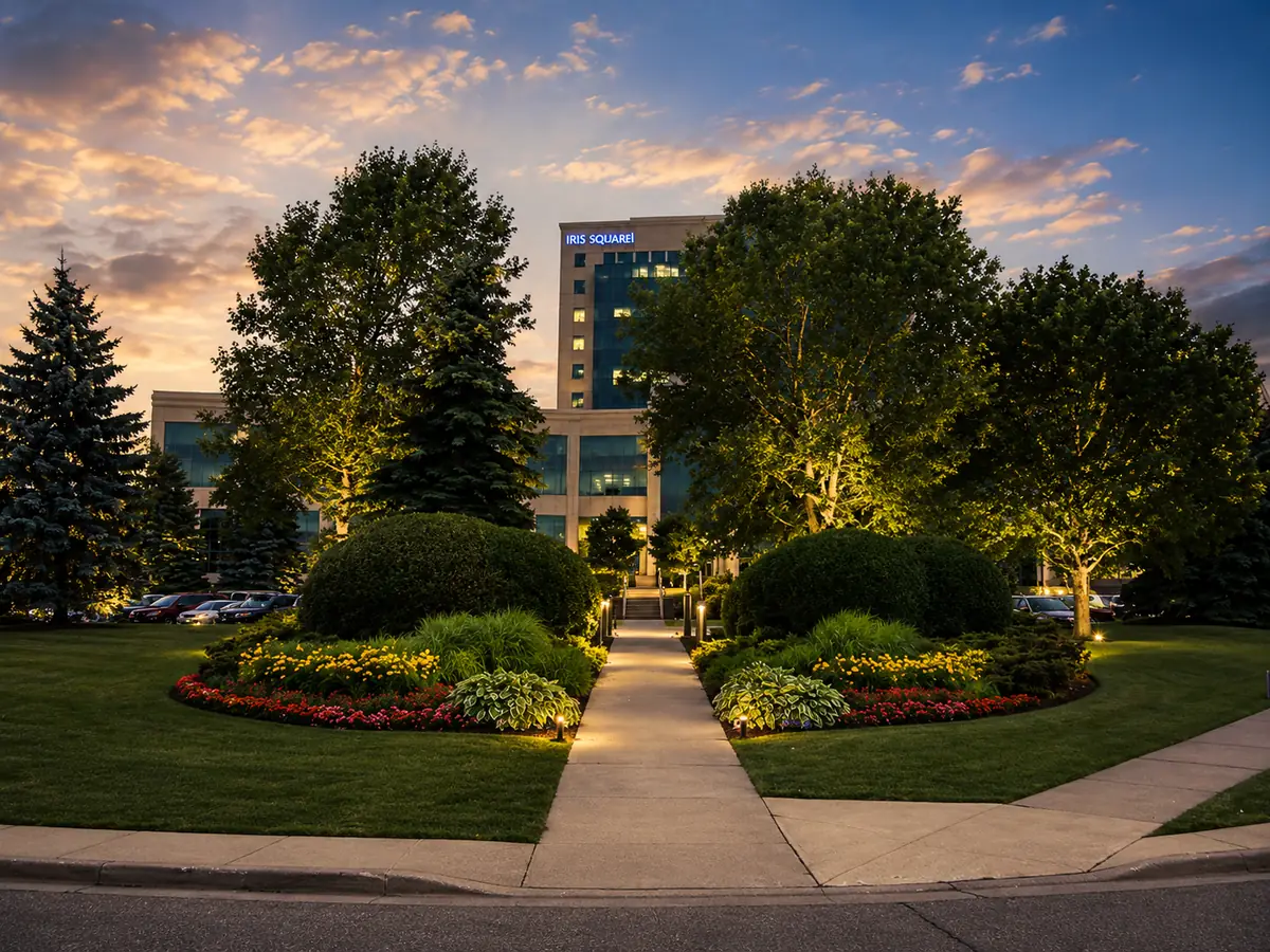 Golden-hour view of a maintained commercial campus walkway with layered planting beds and mature trees.