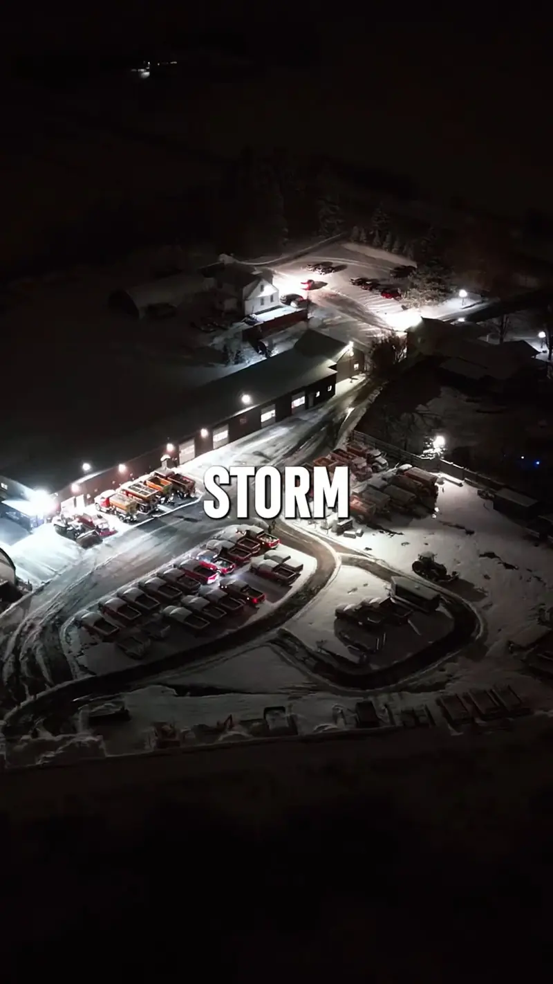 Aerial view of the yard during a winter storm, equipment lit and positioned for overnight deployment.
