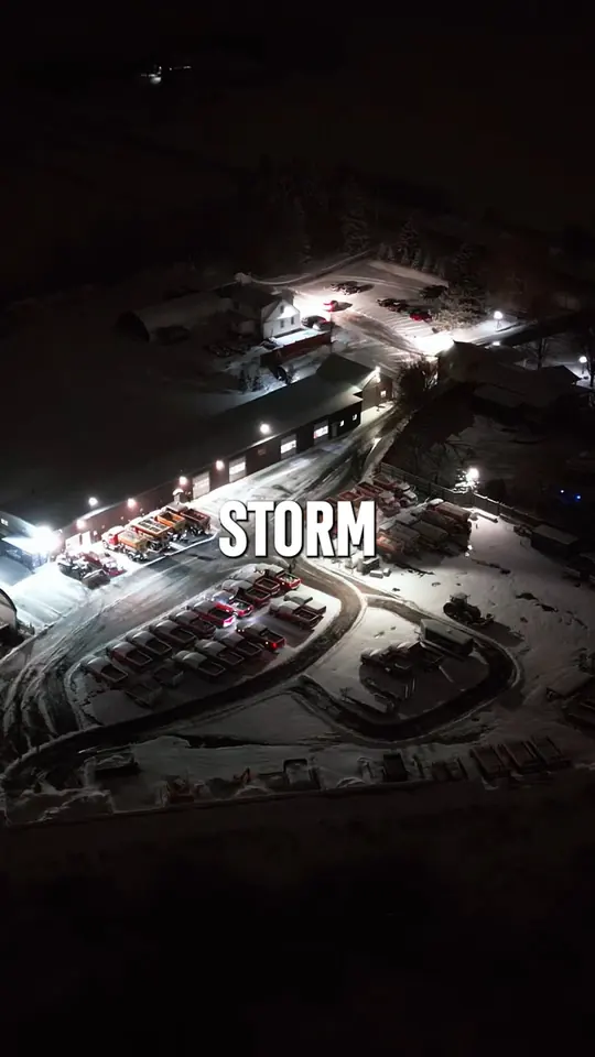 Night aerial of the yard mid-storm with equipment lit and ready to deploy.
